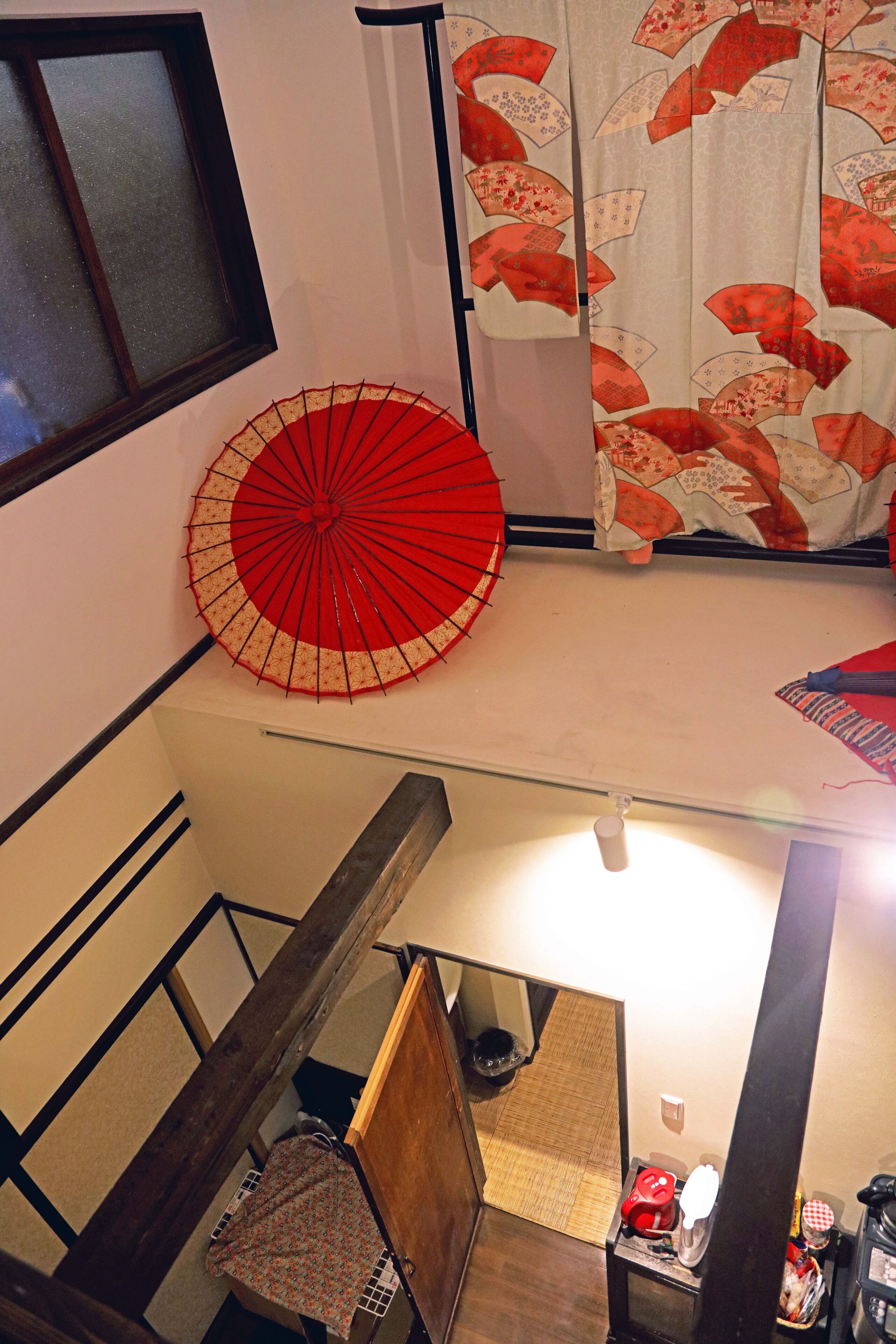 Una escalera con barandilla de madera, un paraguas rojo y un tradicional puertas correderas japonesas.