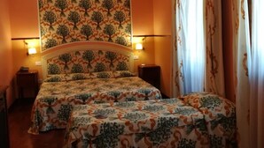 Una habitación con dos camas, un cabecero estampado, lámparas de pared y cortinas.
