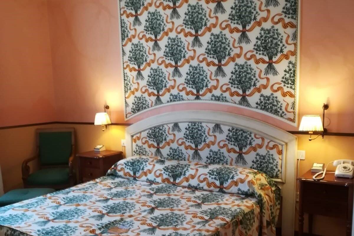 A hotel room with a large bed, two bedside tables, a green chair, and a wall with a tree pattern.
