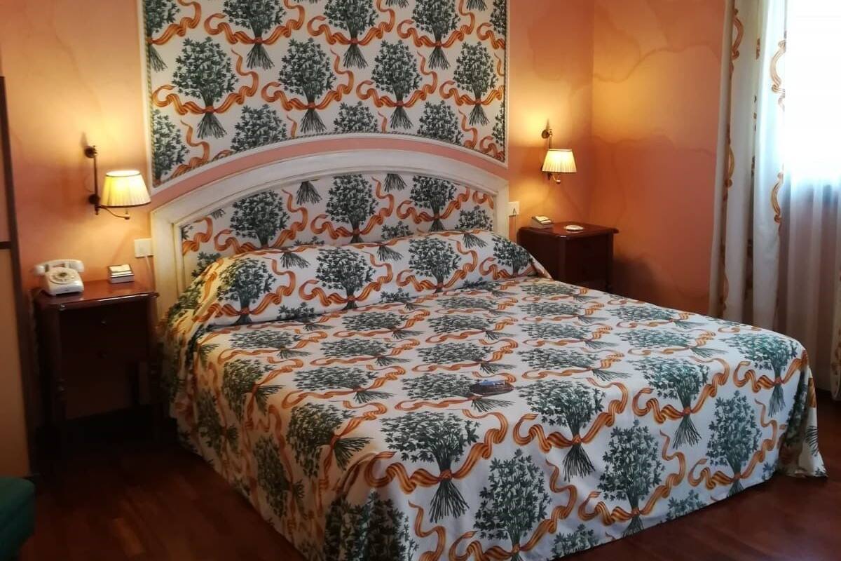 A bedroom with a patterned bedspread, a headboard, two bedside tables with lamps, a telephone, and a window with curtains.