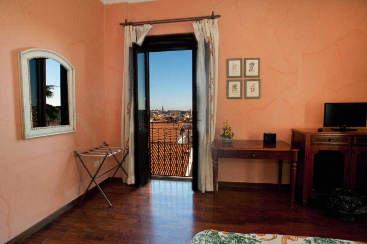 A room with a balcony, a drying rack, a small table with a vase, a TV, and a cabinet.