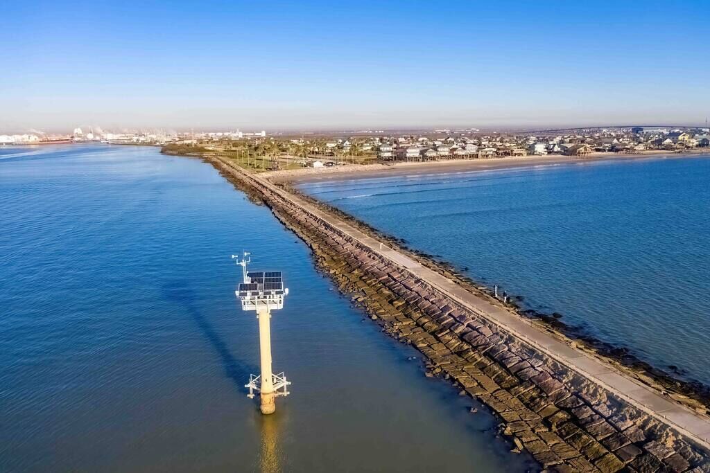 Une zone côtière comprenant un phare, une digue et, au loin, une zone résidentielle.