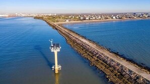 Une zone côtière comprenant un phare, une digue et, au loin, une zone résidentielle.