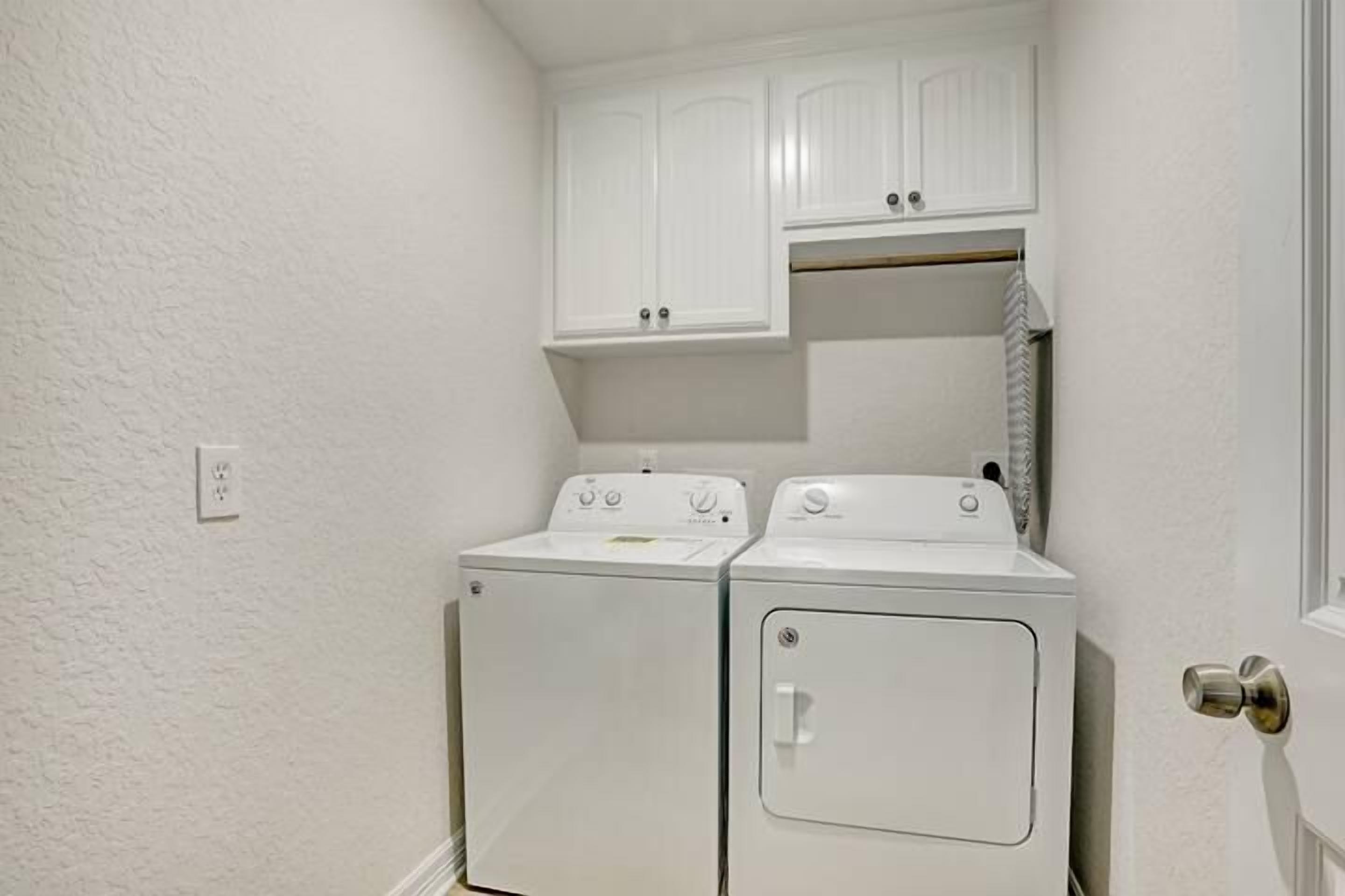 Une buanderie avec deux sèche-linge blancs et un meuble de rangement au-dessus.
