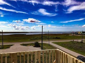 Una terraza de madera con vistas a un lago y una carretera que lleva a un pequeño poblado.