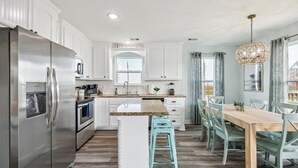 A modern kitchen with white cabinetry, a stainless steel refrigerator, a wooden island, and a dining area with light blue chairs. - 🌴Surfside Paradise#3-amazing views,golfcart🌴 (Surfside Beach)