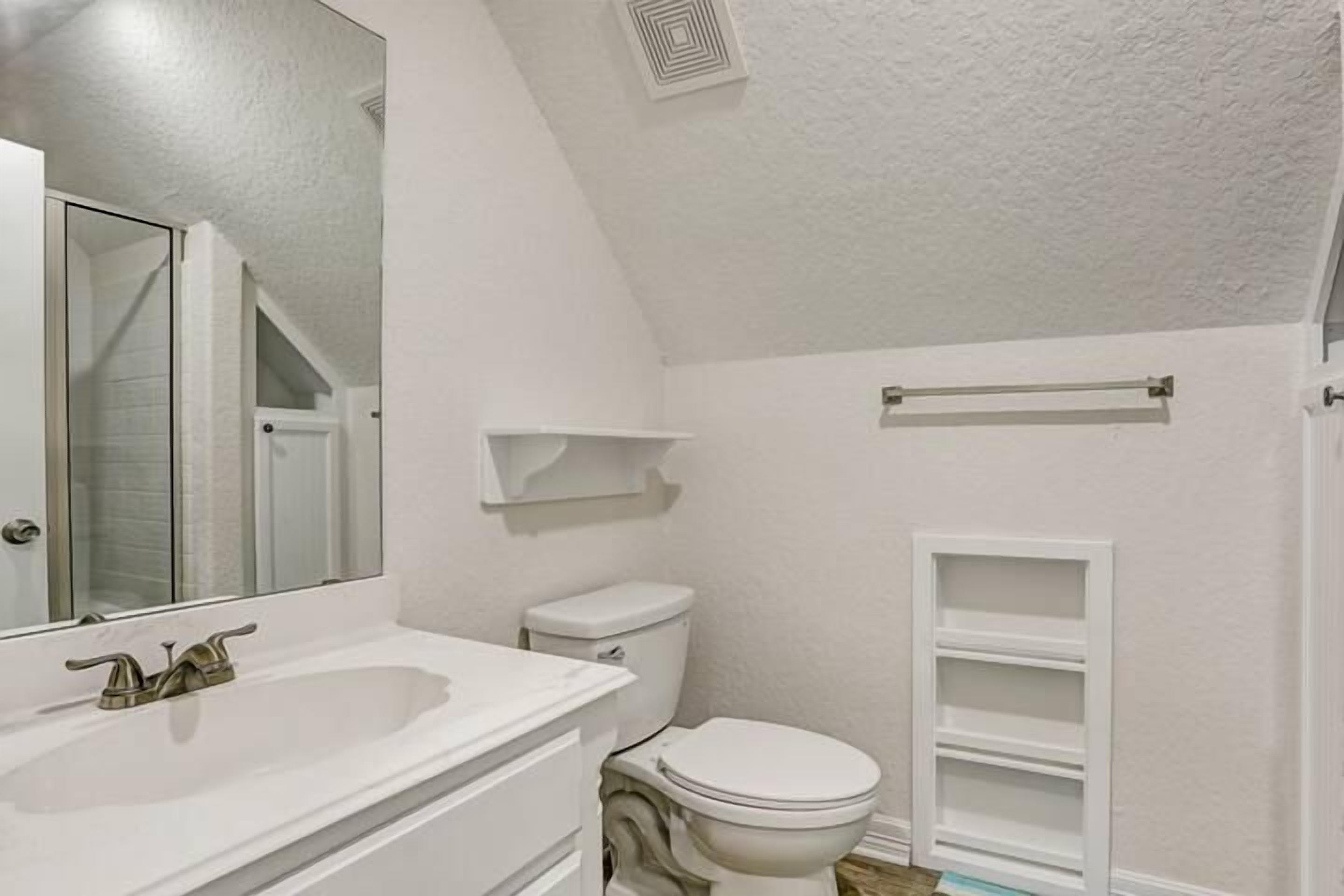 Une salle de bain avec un lavabo blanc, des toilettes et un miroir.