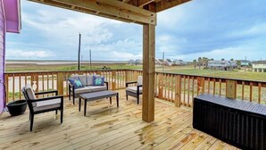 A wooden deck with outdoor furniture, including chairs and a sofa, overlooking a grassy area with houses in the distance. - 🌴Surfside Paradise#3-amazing views,golfcart🌴 (Surfside Beach)