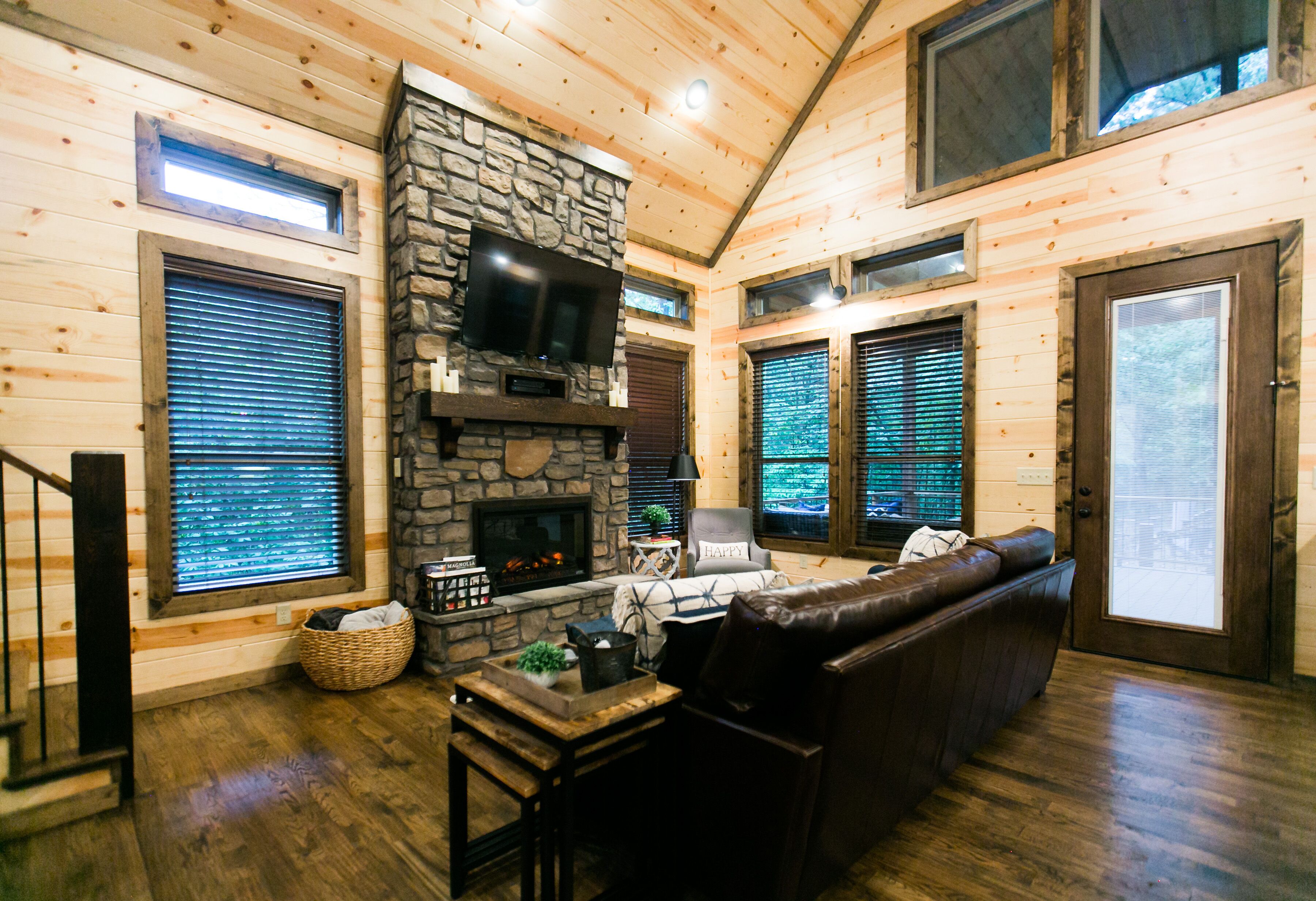 A cozy cabin interior with a stone fireplace, leather sofa, and wooden walls.