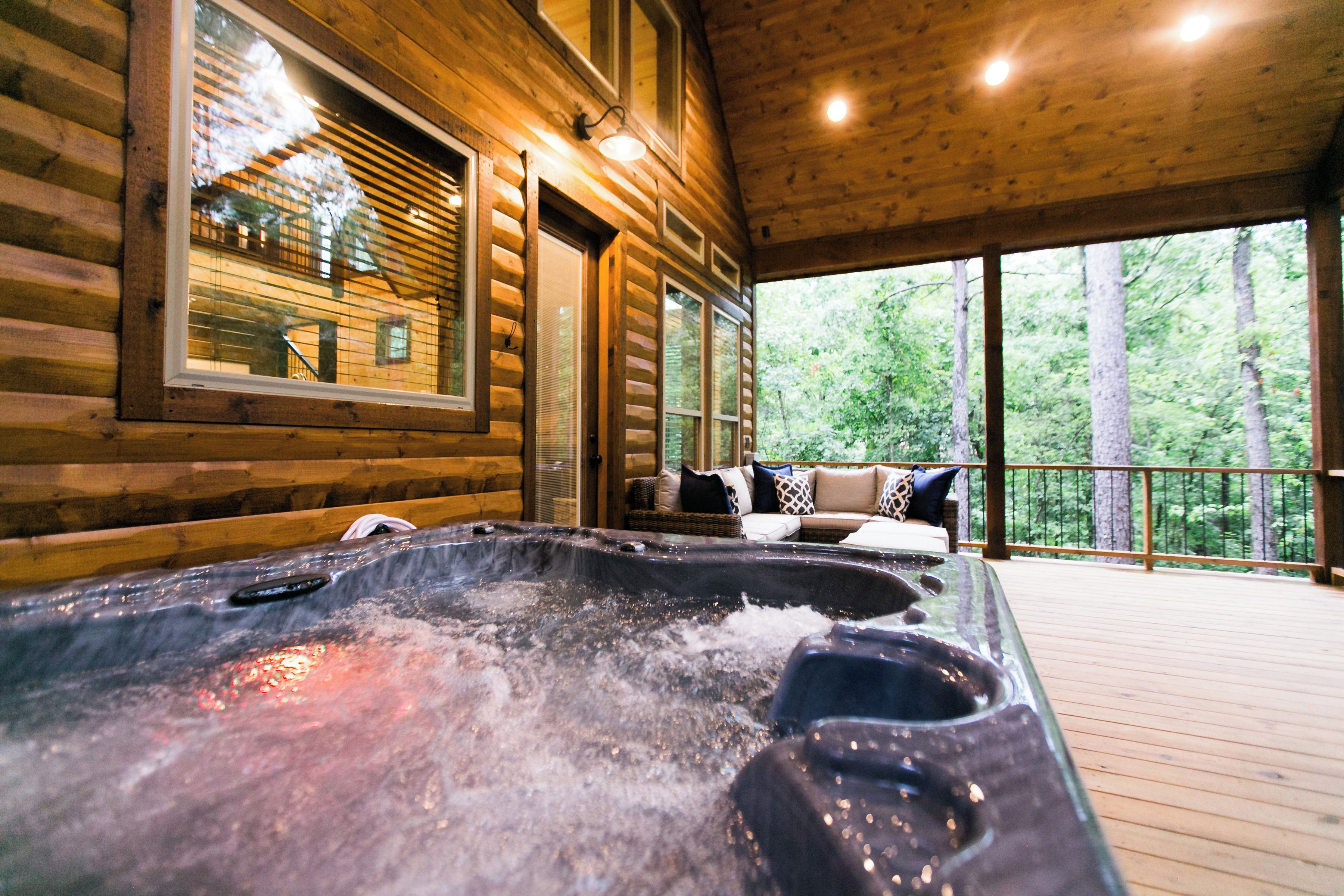 Una cabaña de madera con jacuzzi y balcón con vistas al bosque.