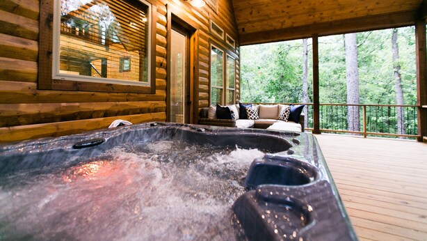 A wooden cabin with a hot tub and a balcony overlooking a forest. - Free at Last- Romantic, Hot Tub, Loft, Free Firewood, Great Location! (Broken Bow)