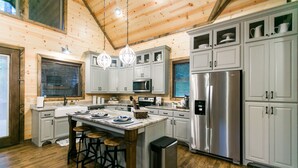 A modern kitchen with wooden walls, stainless steel appliances, and a central island with stools. - Free at Last- Romantic, Hot Tub, Loft, Free Firewood, Great Location! (Broken Bow)