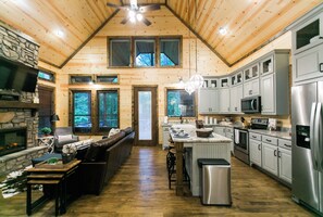 A spacious kitchen with wooden walls, a stone fireplace, and modern appliances.