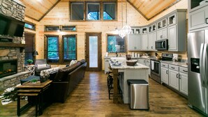 A spacious kitchen with wooden walls, a stone fireplace, and modern appliances. - Free at Last- Romantic, Hot Tub, Loft, Free Firewood, Great Location! (Broken Bow)