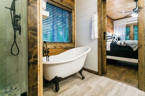 A bathroom with a clawfoot bathtub, wooden walls, a window with blinds, and a shower area. - Free at Last- Romantic, Hot Tub, Loft, Free Firewood, Great Location! (Broken Bow)