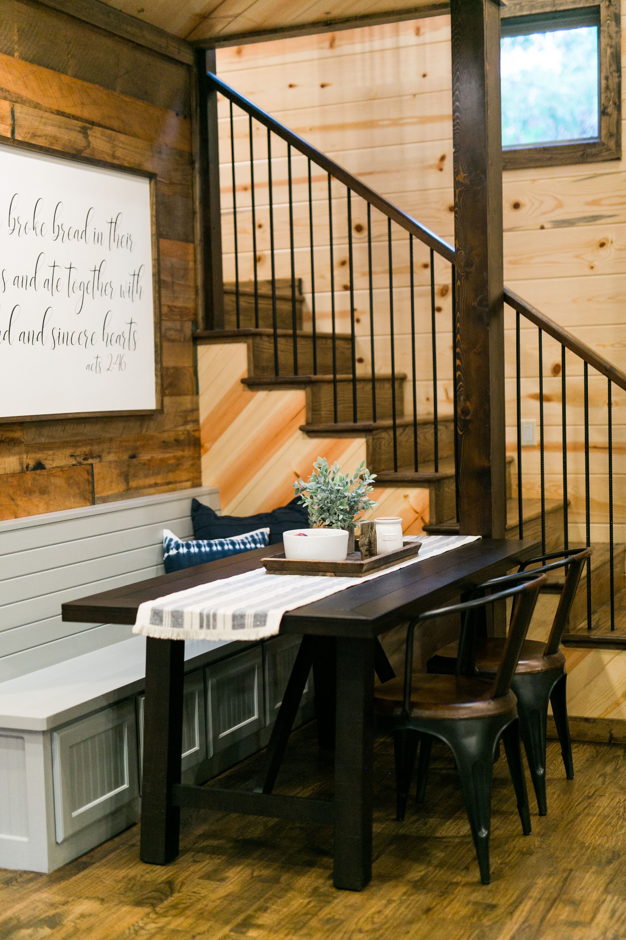 A wooden interior with a dining table set for four, a bench, and a staircase with a railing.