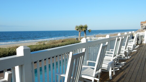 A wooden deck with white rocking chairs overlooking a beach. - Across The Street From The Beach, Private Beach & Pool Access, Elevator (Holden Beach)