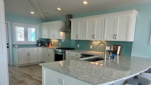 A modern kitchen with white cabinets, a granite countertop, and a stainless steel range hood. - Across The Street From The Beach, Private Beach & Pool Access, Elevator (Holden Beach)