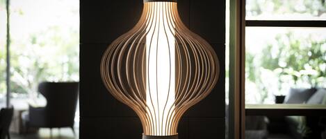 A modern, illuminated floor lamp with a unique, ribbed design in a contemporary room with large windows and a view of greenery outside.