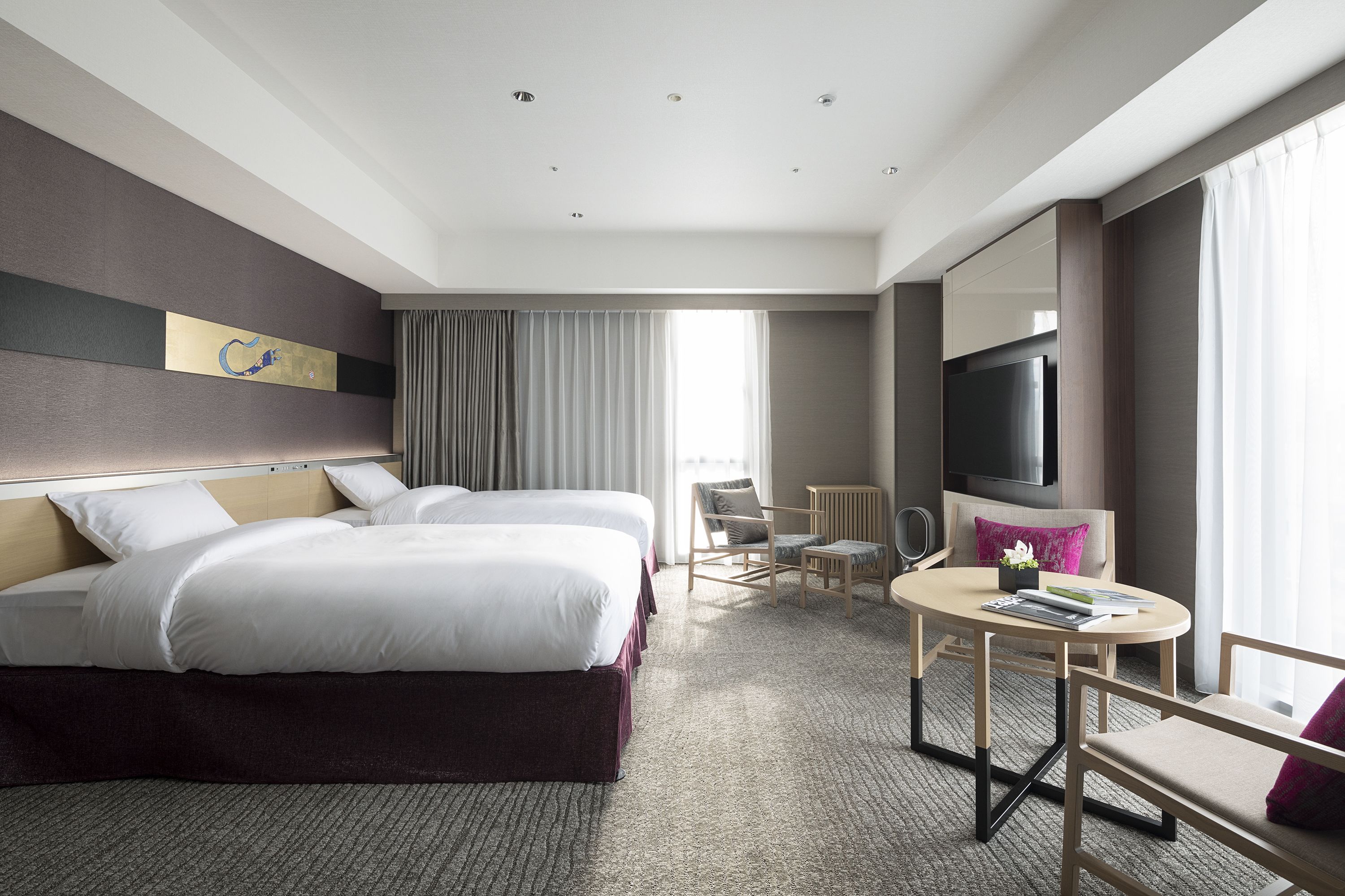 A hotel room with two beds, a round table with chairs, a TV, and a large window with curtains.