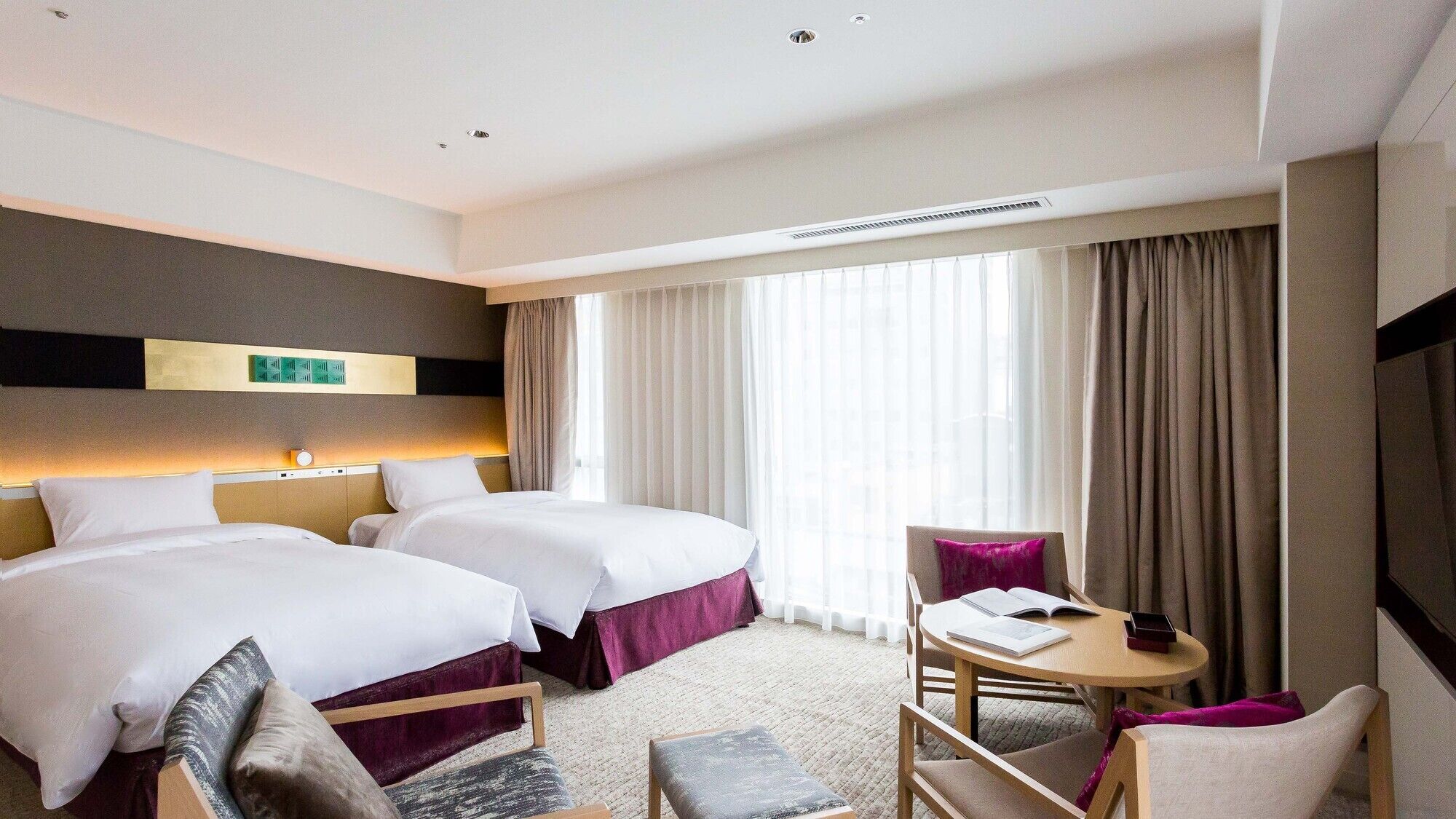 A hotel room with two beds, a desk, and a chair.