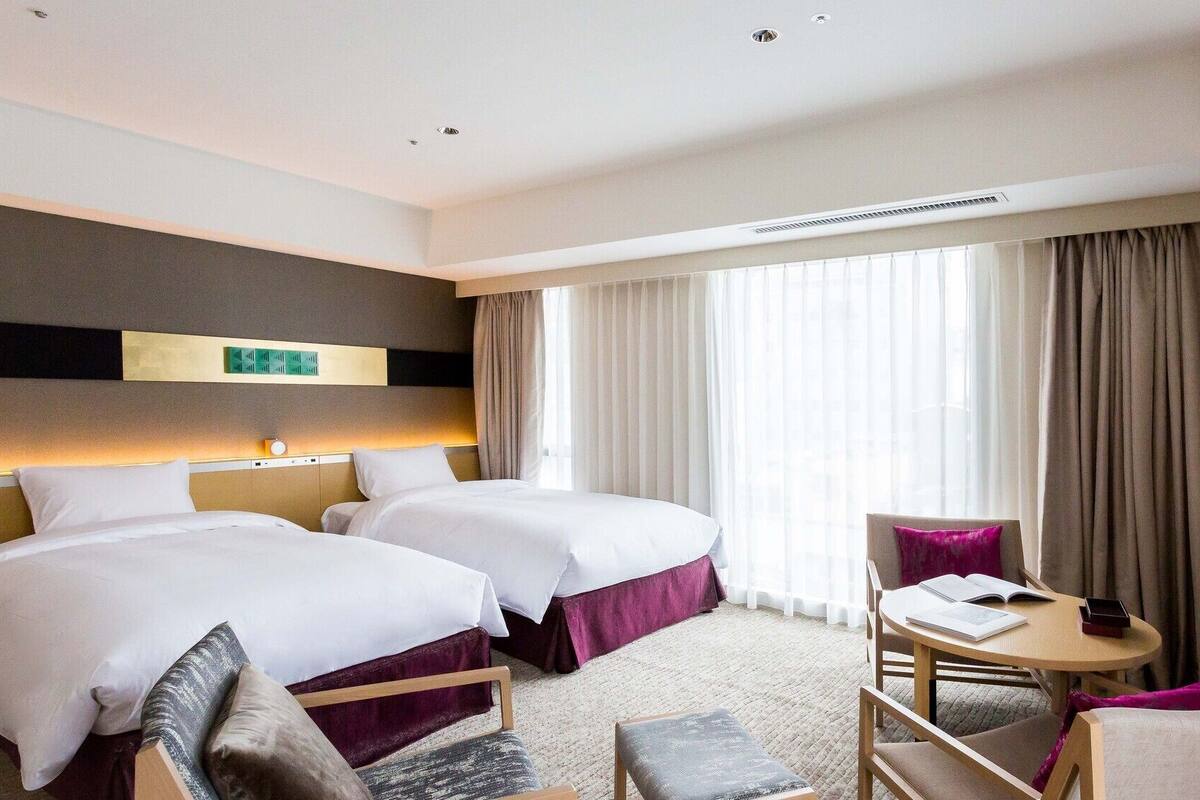 A hotel room with two beds, a desk, and a chair.