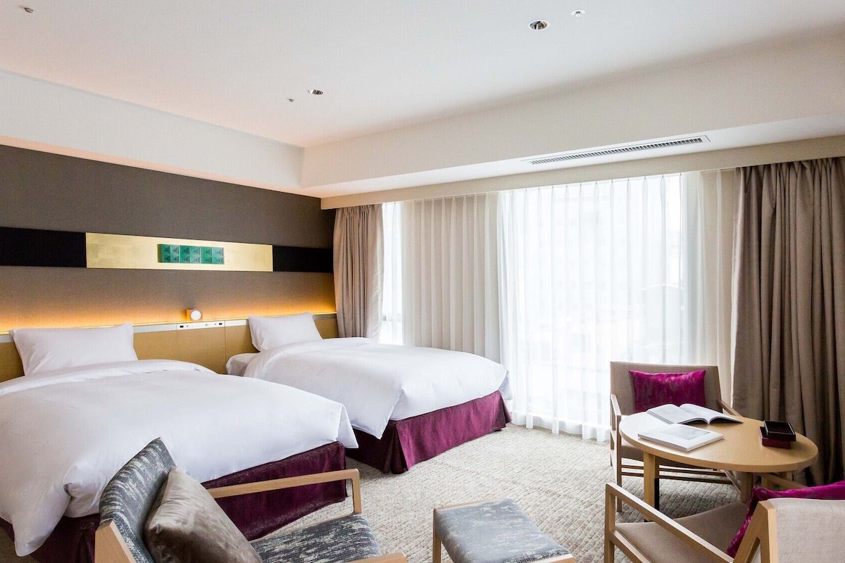 Habitación de hotel con dos camas, un escritorio y una silla.