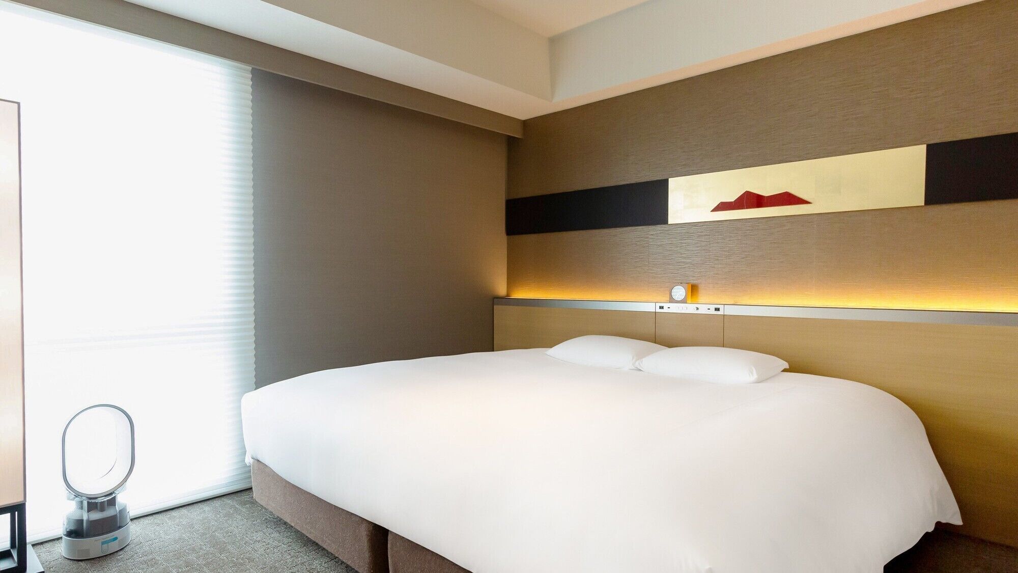 A hotel room with a large bed, a bedside table, a mirror, and a wall-mounted clock.
