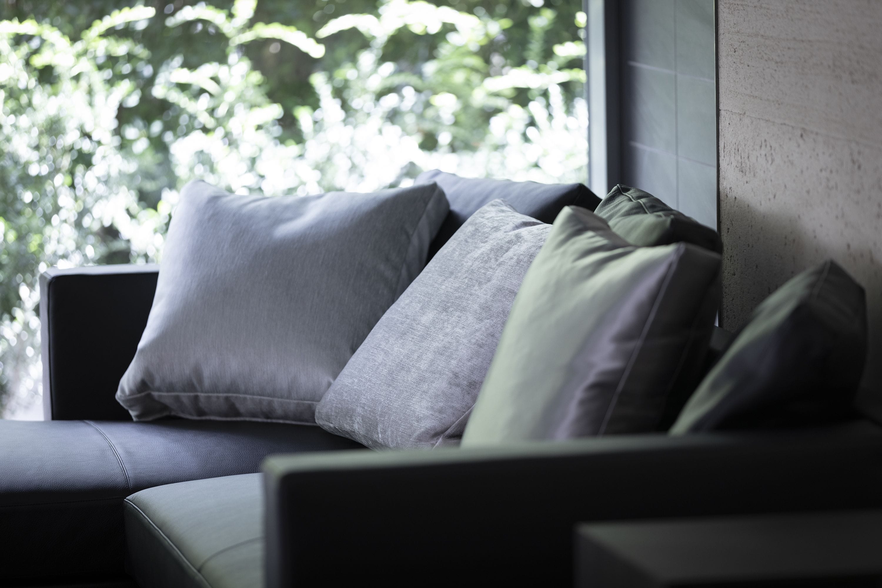 Ein modernes Sofa mit vielen Kissen in einem Raum mit einem großen Fenster.