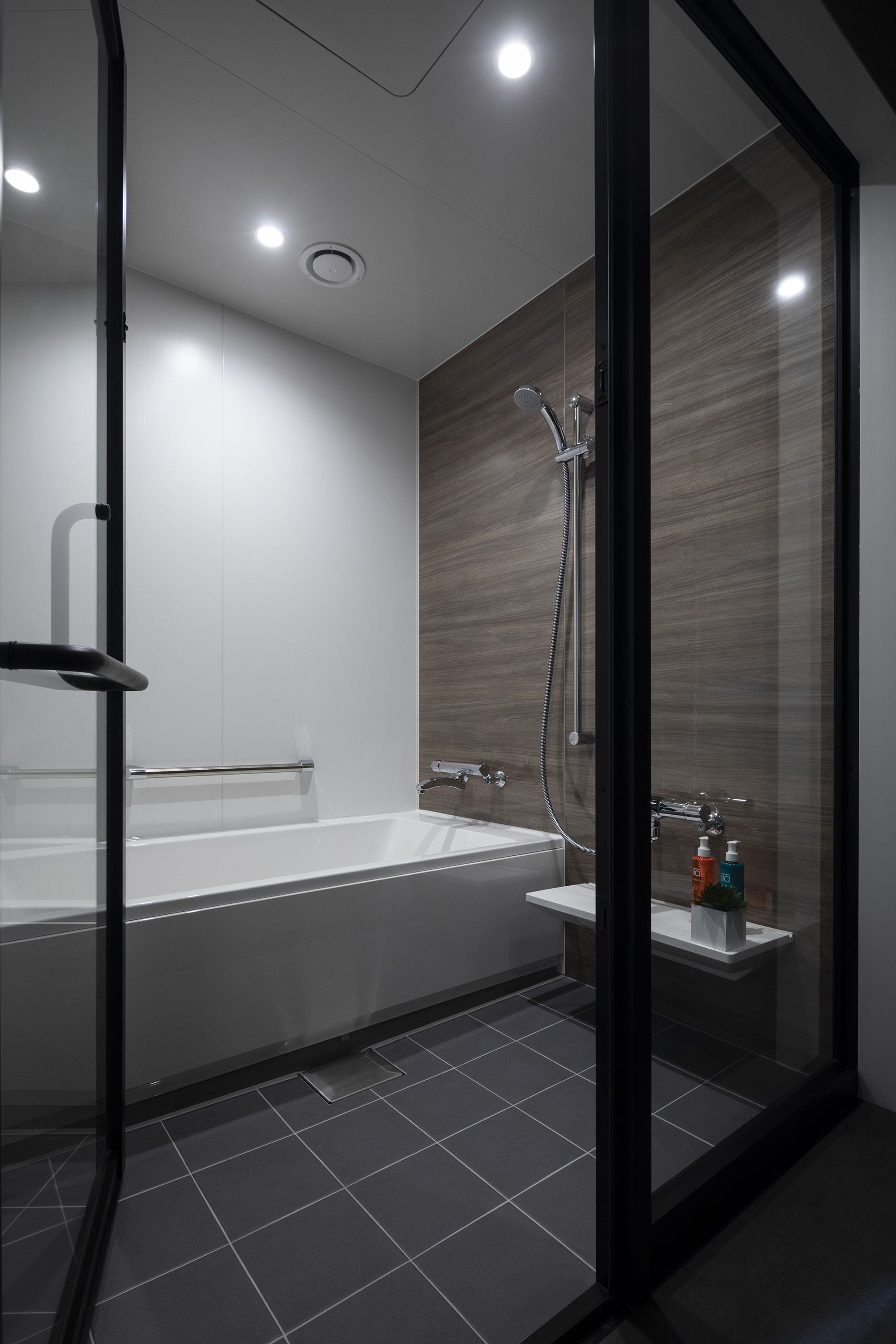 Un baño moderno con ducha envuelta en vidrio, una bañera blanca y un estante pequeño con artículos de aseo.