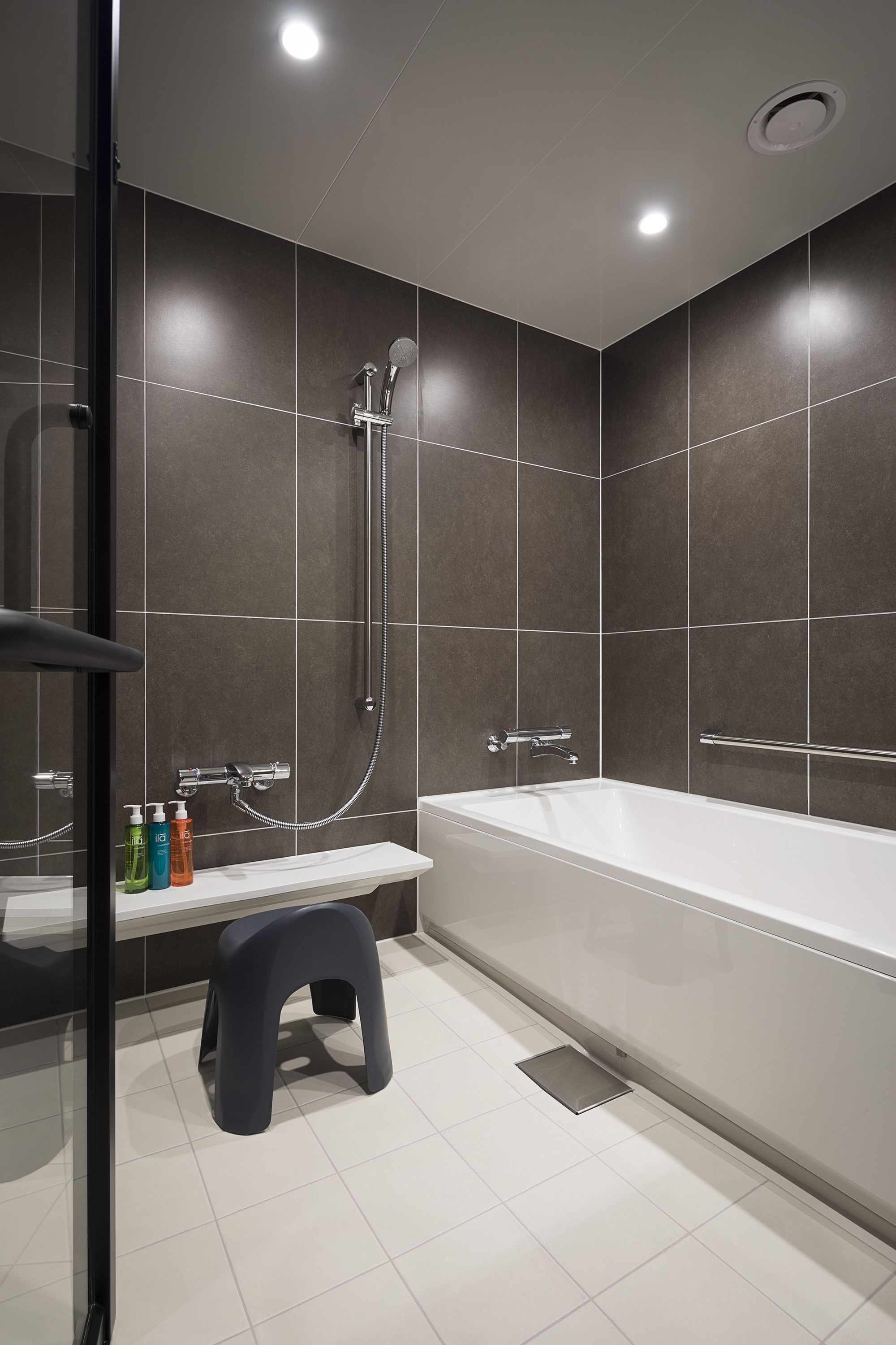 Une salle de bain moderne équipée d’une baignoire, d’une douche et d’un petit tabouret sur lequel sont posés les articles de toilette.