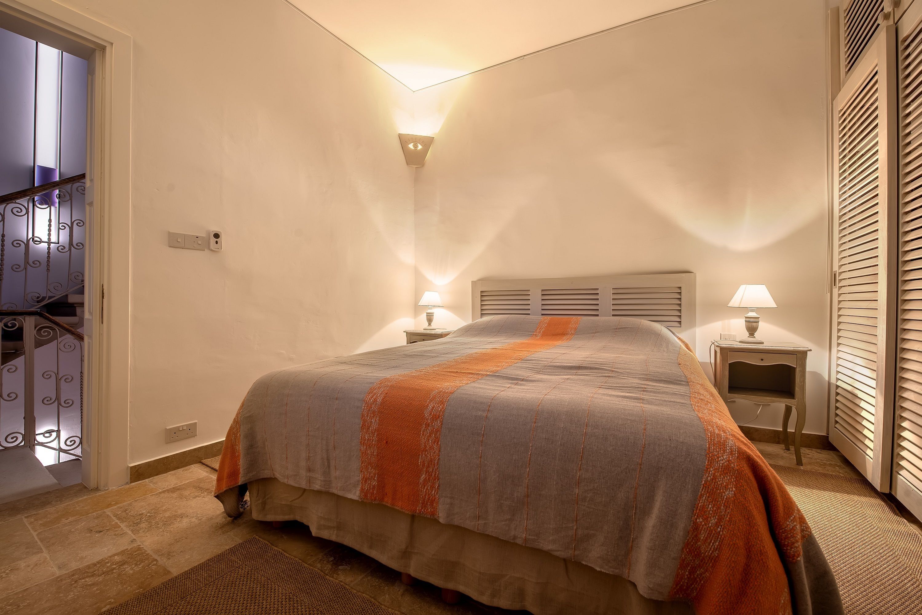 Ein Schlafzimmer mit einem Bett, Nachttischlampen, einem Nachttisch und einer Tür mit einer dekorativen Geländer.