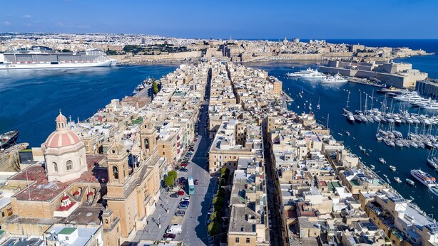 A coastal cityscape with a prominent cathedral, a bustling harbor, and a clear view of the sea. - The Snop House (Senglea)