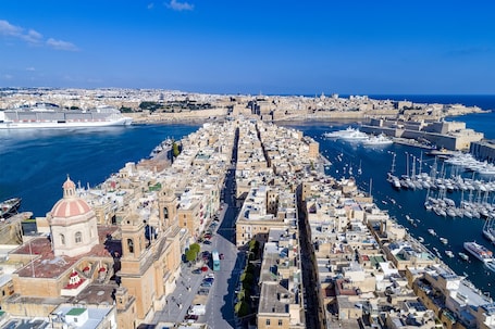A coastal cityscape with a prominent cathedral, a bustling harbor, and a clear view of the sea.
