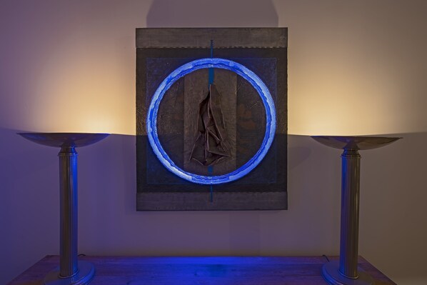 A framed artwork with a circular blue light effect, displayed on a wall between two floor lamps. - The Snop House (Senglea)