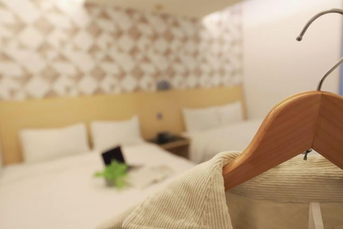Una camera d'albergo con un letto, un appendiabiti in legno e una parete decorata.