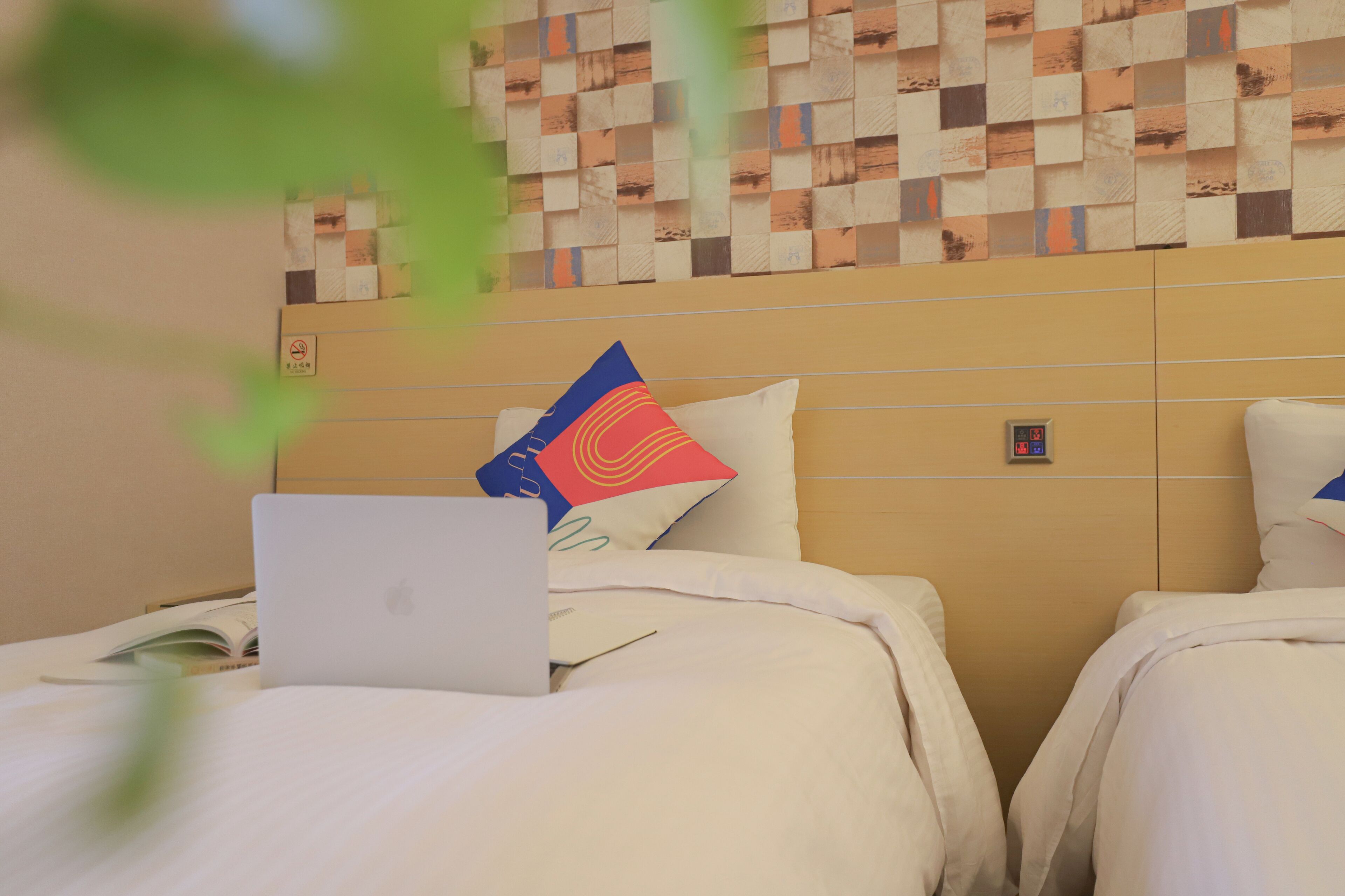 Habitación de hotel con dos camas, una laptop sobre una de ellas, y una pared con diseño decorativo.