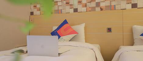 Habitación de hotel con dos camas, una laptop sobre una de ellas, y una pared con diseño decorativo.