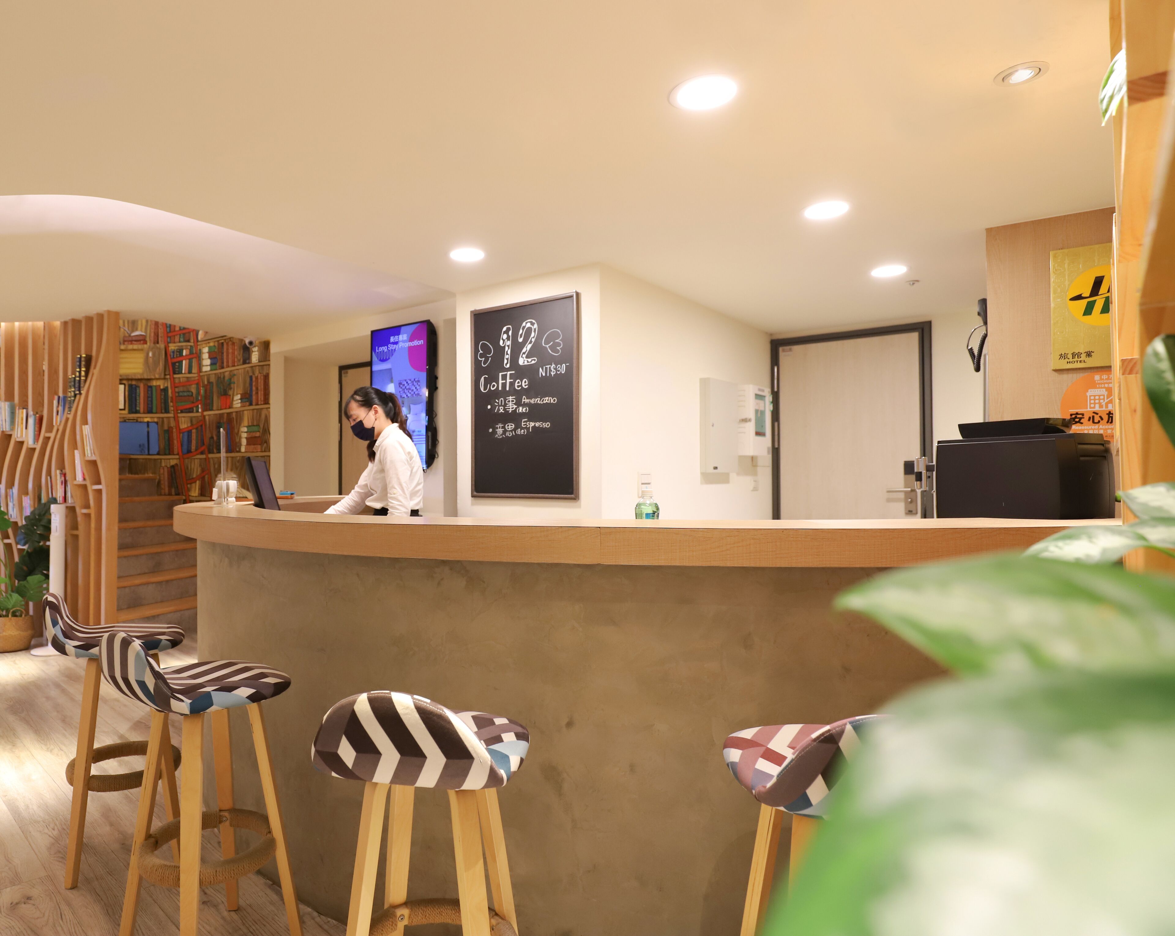 A reception area with a counter, a woman behind it, a coffee menu, and a bookshelf.