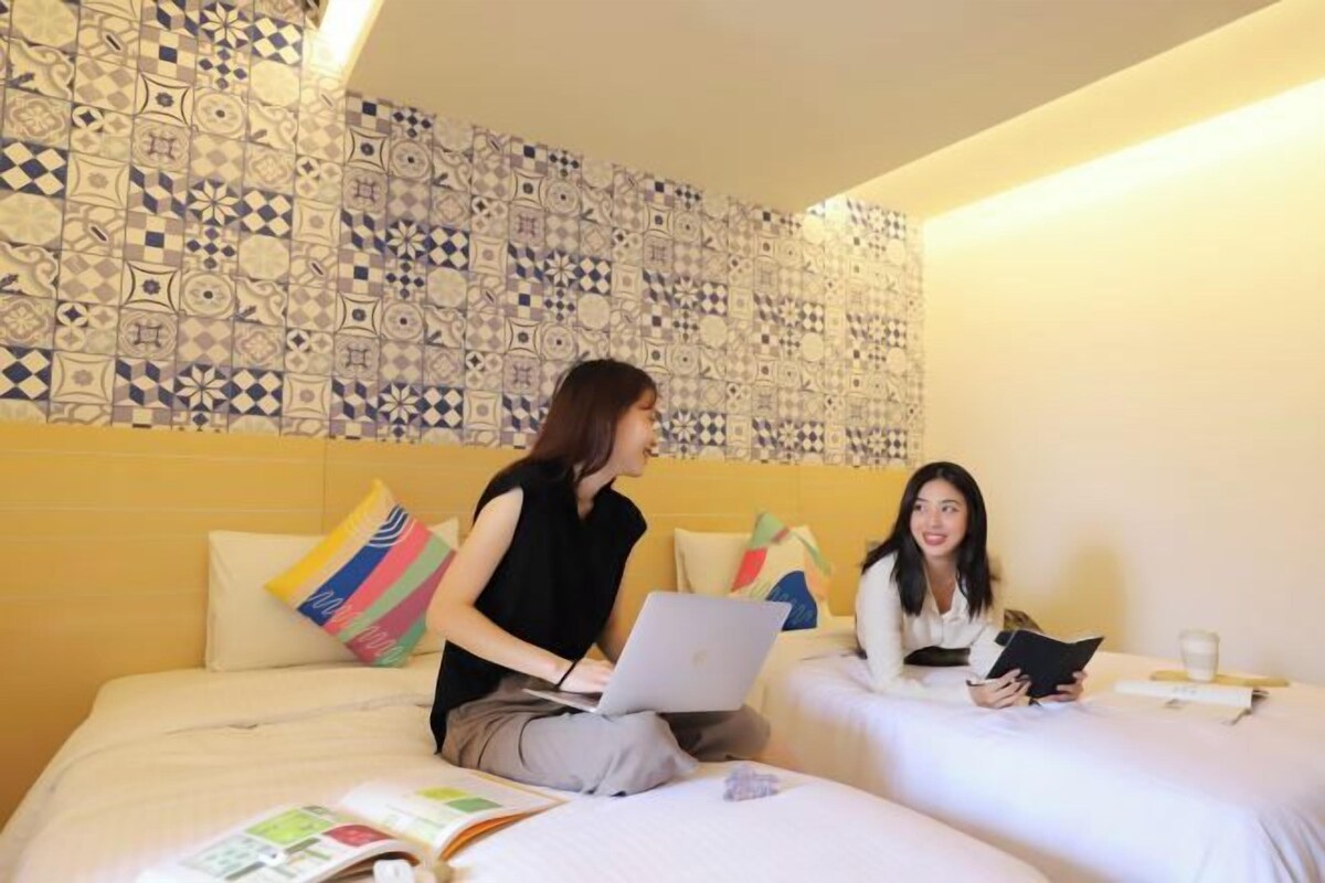 Camera d'albergo con due letti, una parete decorata e un portatile su un letto.