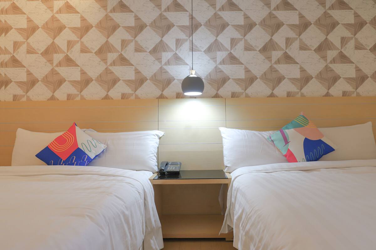 Habitación de hotel con dos camas, una mesita de noche y pared con estampado geométrico.