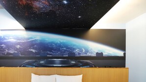 A bedroom with a bed, a wooden headboard, and a large wall-mounted screen displaying a space scene.