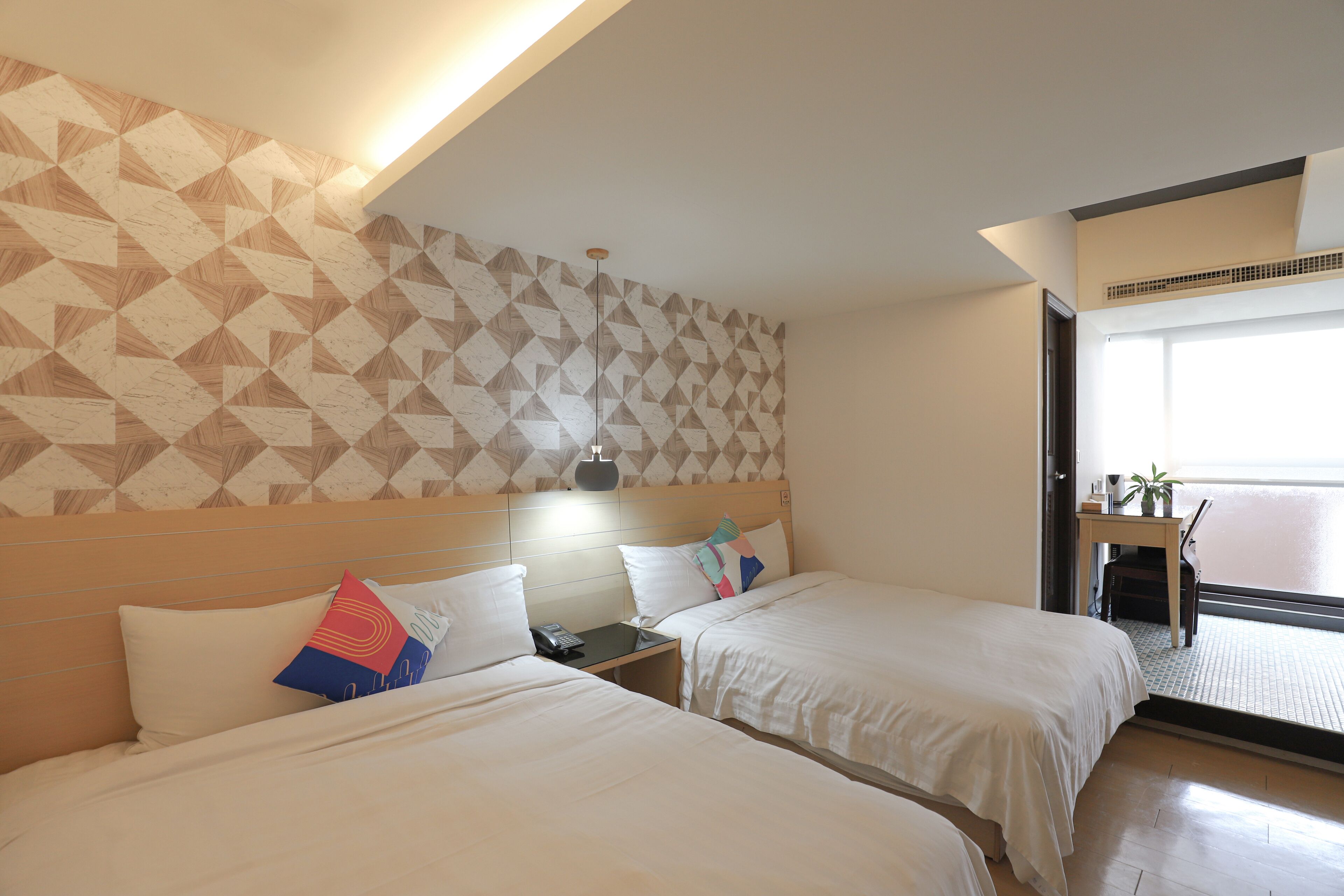 A hotel room with two beds, a desk, and a view of the outside.