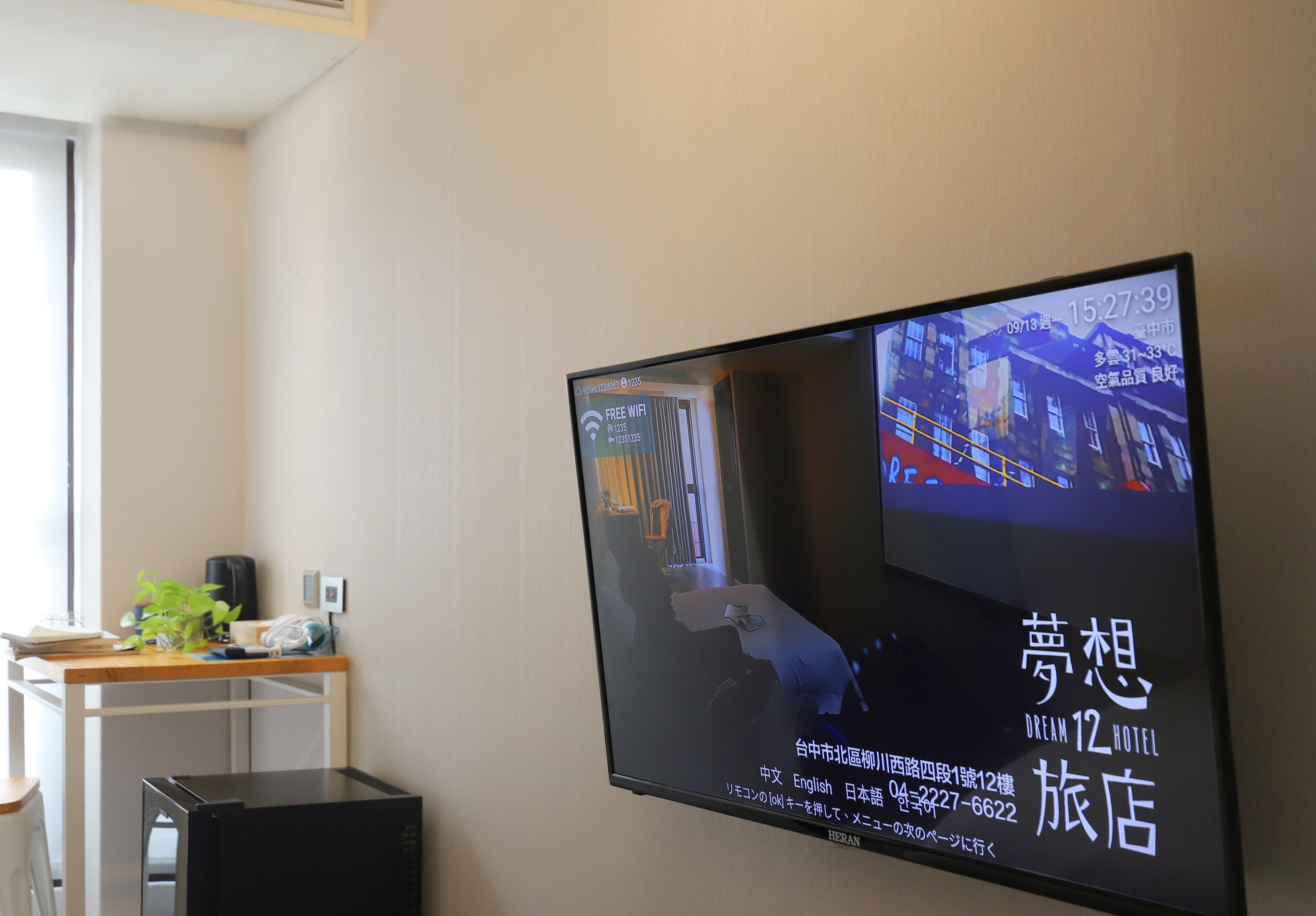 A television displaying a hotel advertisement with a room layout, a desk with a plant, and a small trash bin.