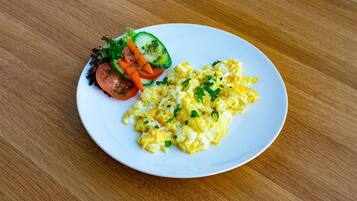 A plate of scrambled eggs with a side salad of lettuce, cucumber, tomato, and carrot.