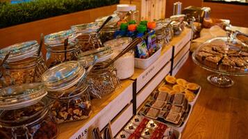 En buffet med forskellige spisemuligheder, herunder glas med nødder, chokolade og kager.