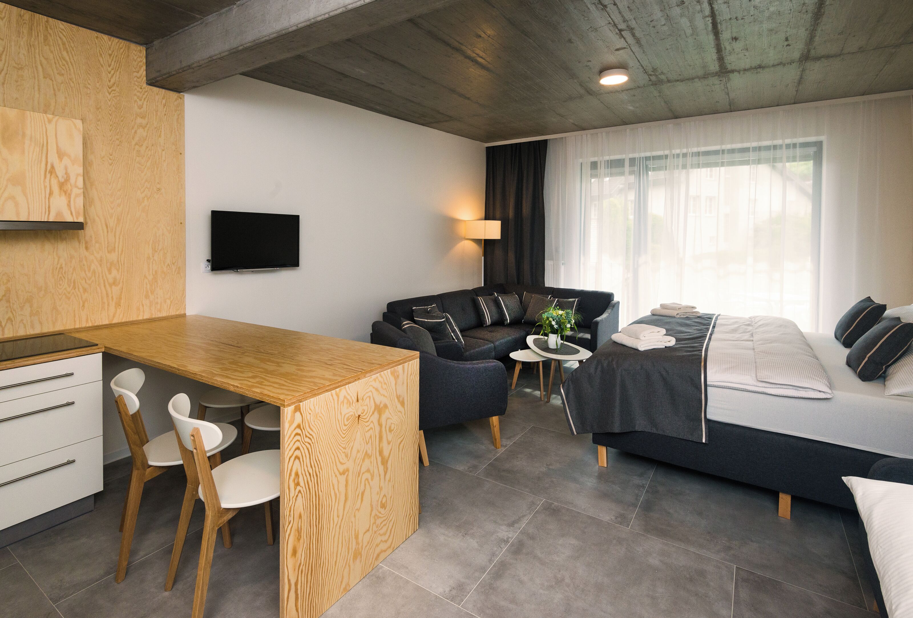 Une chambre d’hôtel moderne avec un bureau en bois, un canapé, un lit et une télévision.