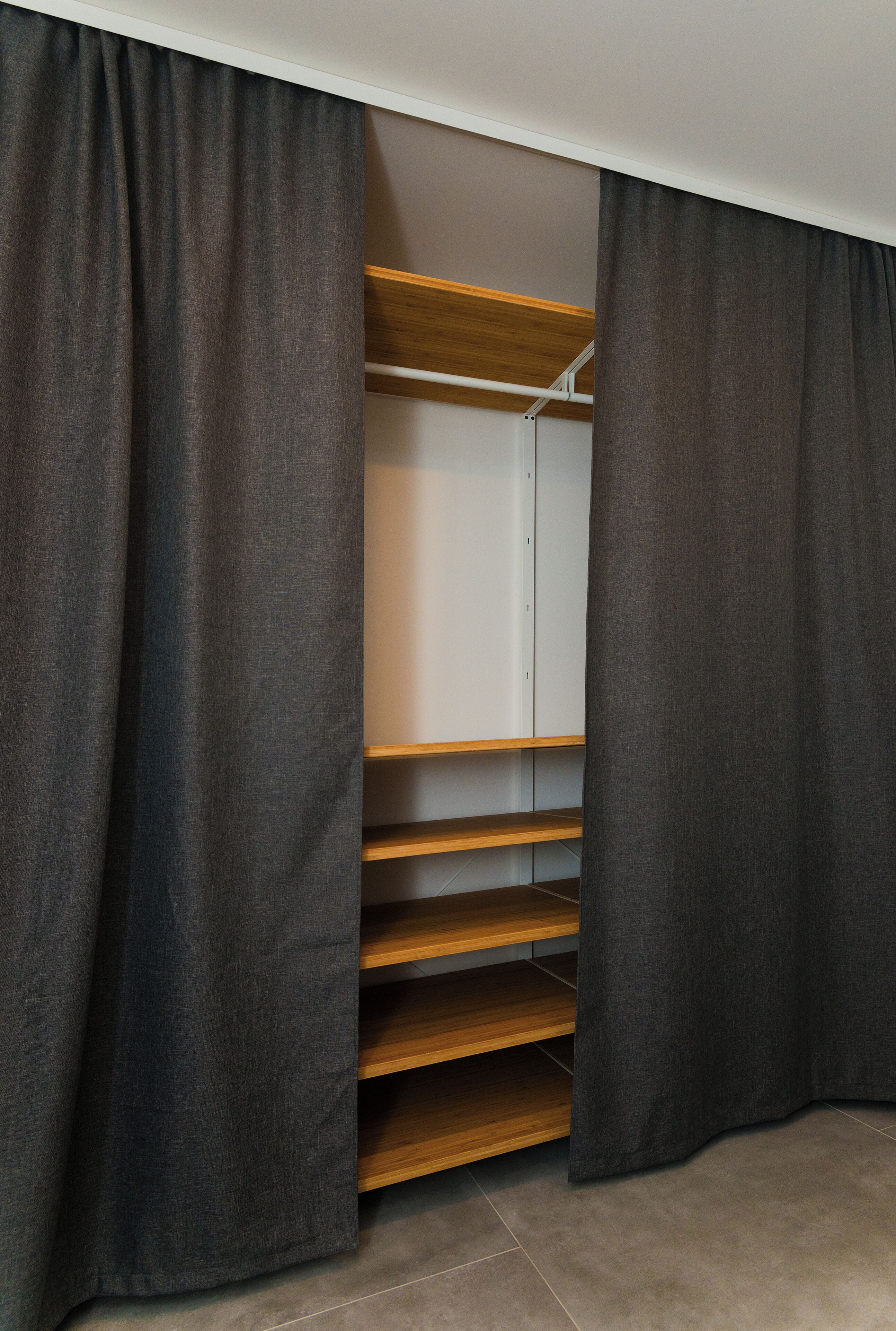 Ein begehbarer Kleiderschrank mit Holzböden und grauen Vorhängen.