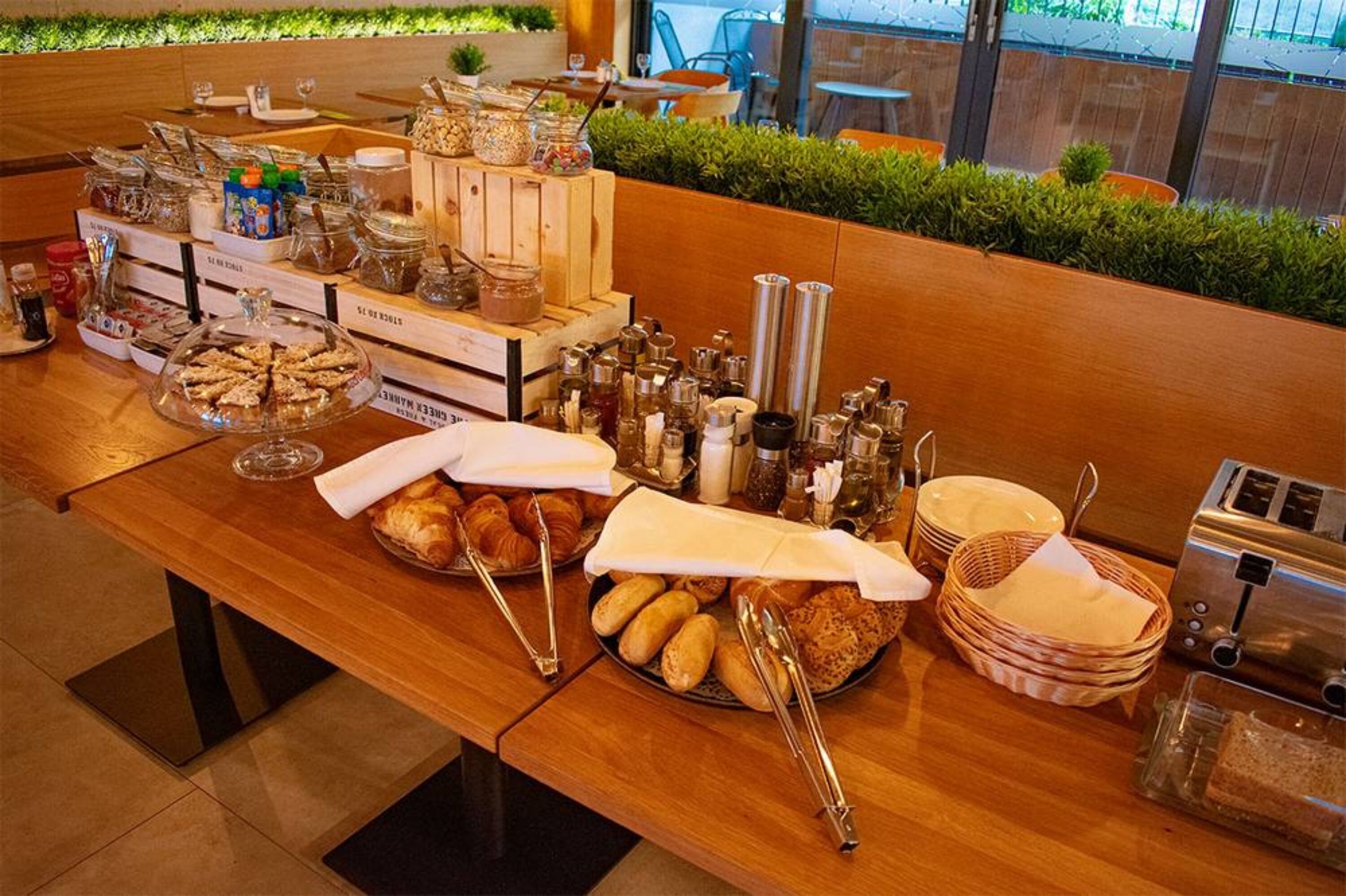 A breakfast buffet with various food items, condiments, and utensils on a wooden table.