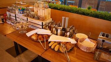 A breakfast buffet with various food items, condiments, and utensils on a wooden table.